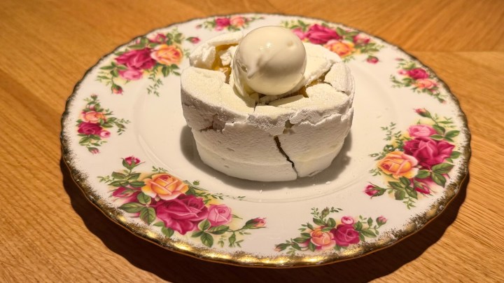 A delicate dessert featuring a cracked meringue shell with a scoop of ice cream on top, served on a floral-patterned plate.