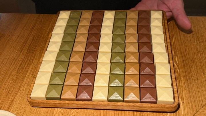 A wooden board displaying an array of colorful chocolates shaped like pyramids, arranged in rows of different hues.