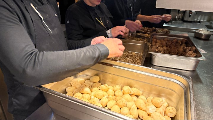 Chefs preparing ingredients in a restaurant kitchen, with a focus on small potatoes and other elements being handled.