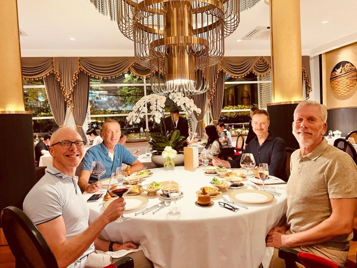 A group of four friends enjoying a fine dining experience at a restaurant with sophisticated decor, elegant table settings, and a chandelier overhead.