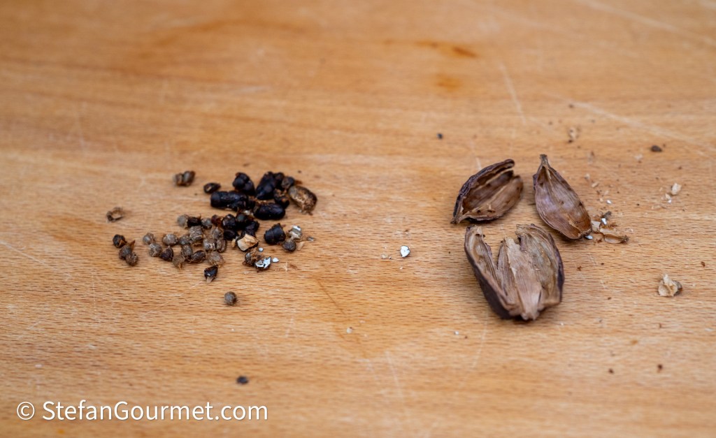 A wooden surface displaying a mix of black cardamom seeds and the empty pods from the cardamom pods.