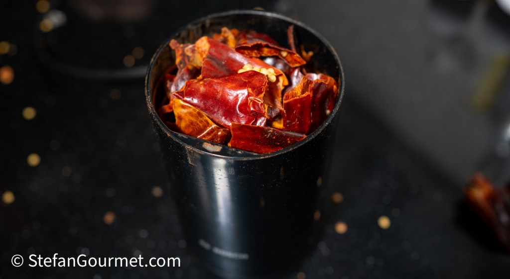 A black spice grinder filled with dried red chili peppers, ready to be ground for a curry paste.