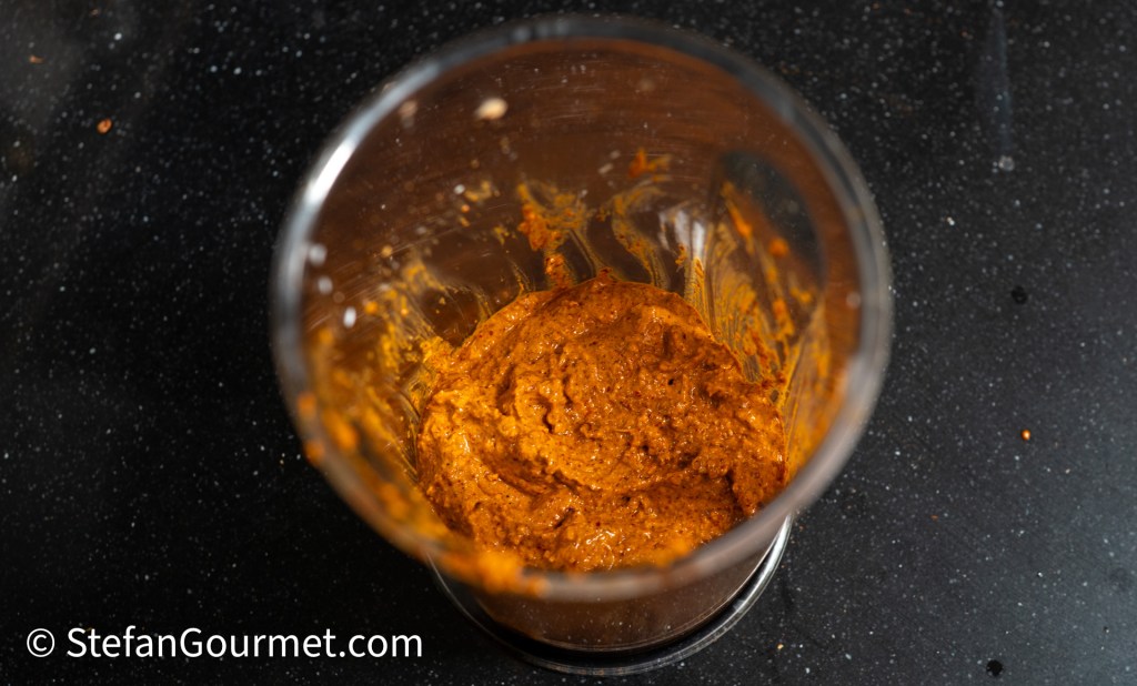 A close-up view of a blender jar containing a thick, orange curry paste, with remnants of the mixture coating the sides.