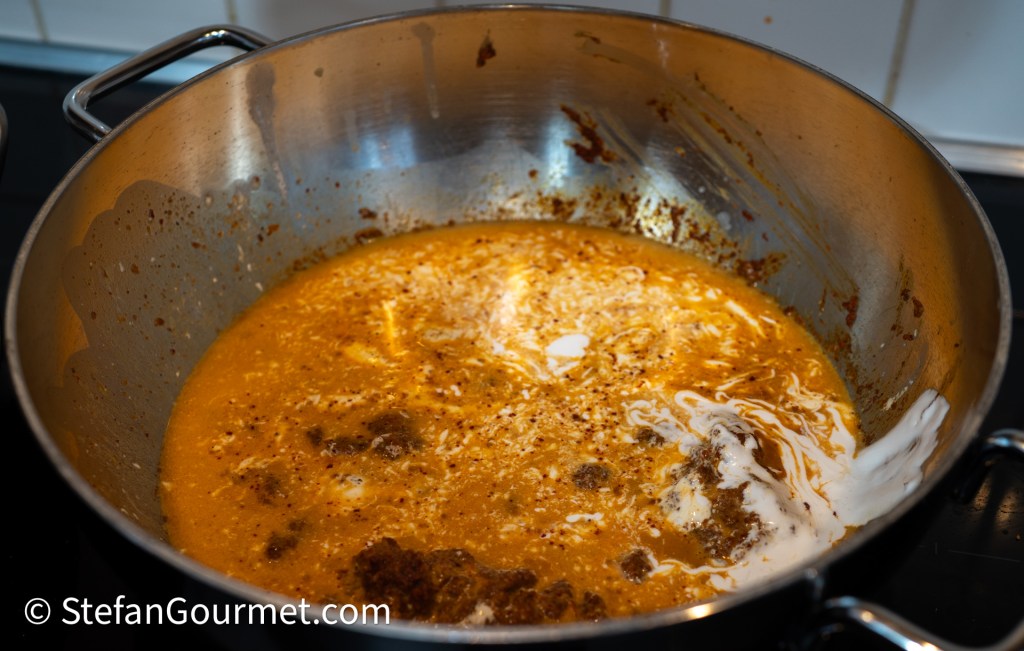 A close-up view of a pot containing a rich curry broth, featuring a creamy texture with swirls of coconut milk and spices, on a stovetop.