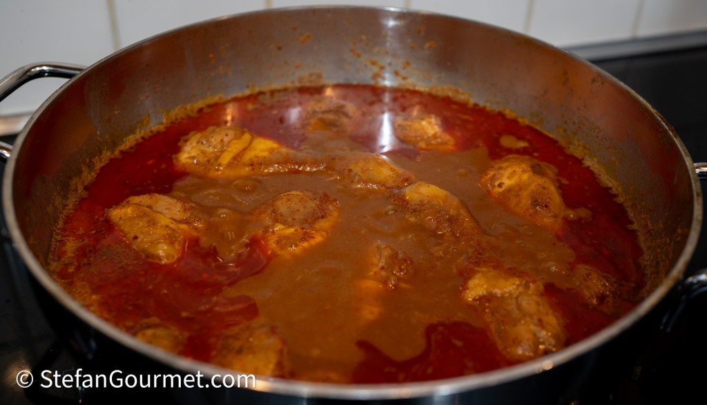 A pot of simmering Khao Soi curry soup with chicken drumsticks and a rich, reddish-brown broth.