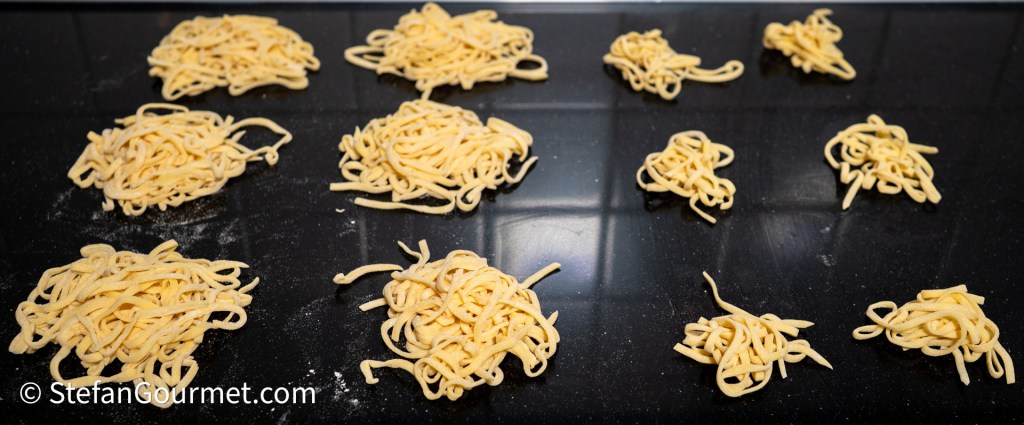 Freshly made egg noodles arranged in small piles on a dark surface, ready for cooking.