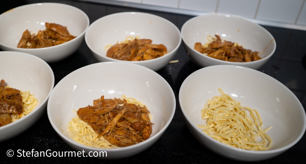 Bowls containing cooked egg noodles and pieces of chicken ready to be served as part of Khao Soi.