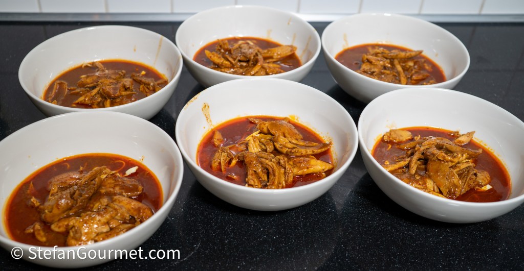 Six white bowls filled with a rich curry broth and shredded chicken, sitting on a dark countertop.