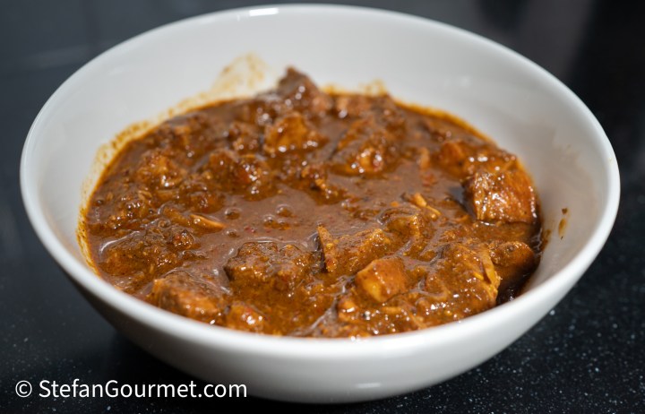 A bowl of Gaeng Hung Lay, a Northern Thai curry with a rich, dark brown sauce and pieces of tender pork.