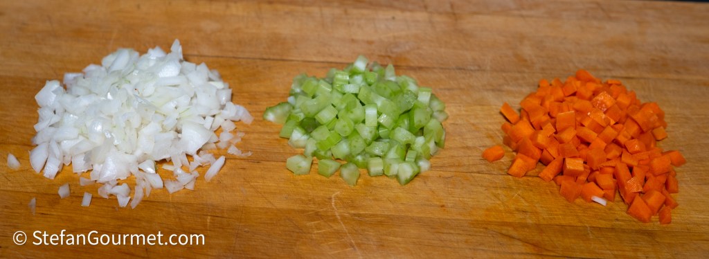 Finely diced onion, celery, and carrot arranged on a wooden cutting board.