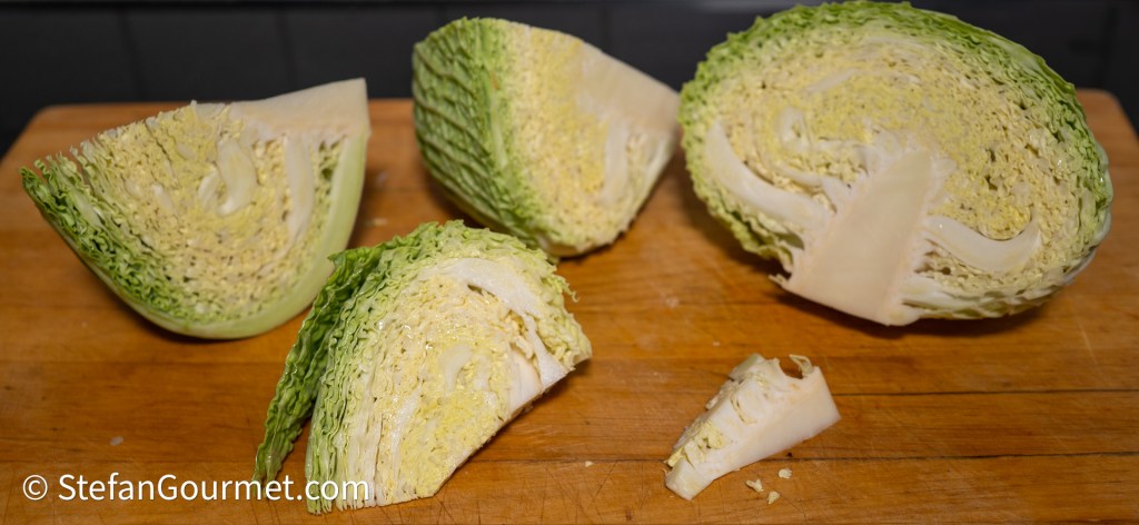 Shredded savoy cabbage on a wooden cutting board, showing cut wedges and the tough core removed.