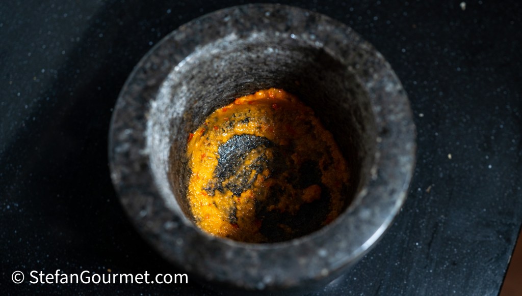 A mortar and pestle containing a colorful paste made from ground spices and ingredients used for a Thai dressing.