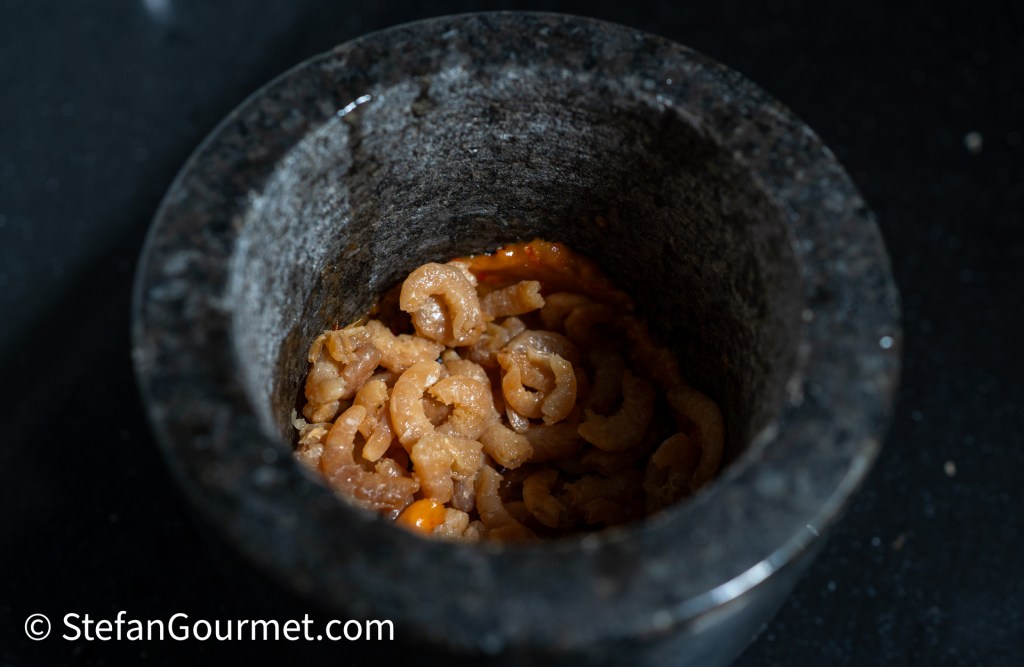 A mortar filled with ground dried shrimp, showcasing their light brown color and texture against the dark stone interior.
