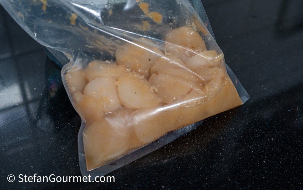 A sealed ziplock bag containing marinated scallops in a light-colored marinade.
