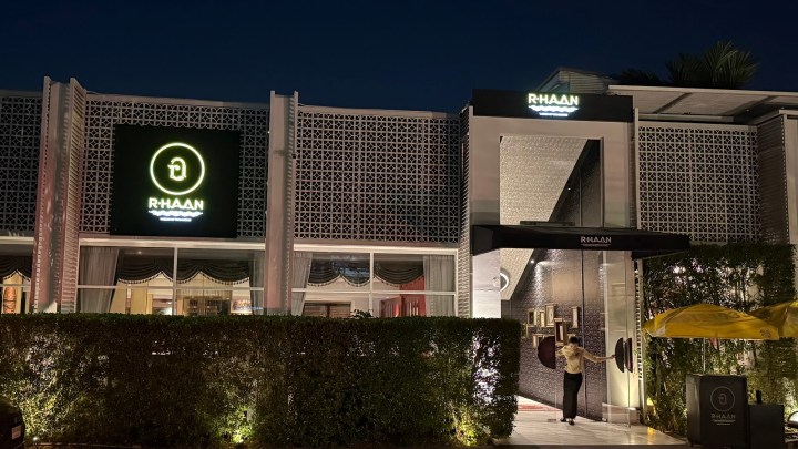 Exterior of R-Haan restaurant at night, featuring a lighted sign and neatly landscaped entrance.
