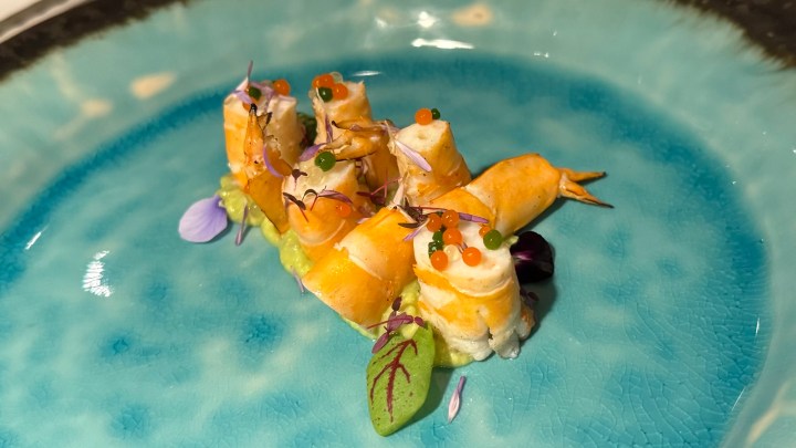 A beautifully plated dish featuring sustainably cultivated Andaman prawns garnished with edible flowers and colorful caviar pearls on a turquoise plate.
