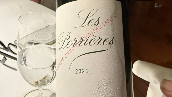 A close-up of a wine bottle labeled 'Les Perrières 2021' beside a glass of water on a white tablecloth.