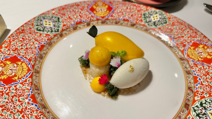 A beautifully presented dessert featuring mango and sticky rice ice cream, garnished with colorful edible flowers and herbs on an ornate Thai-style plate.