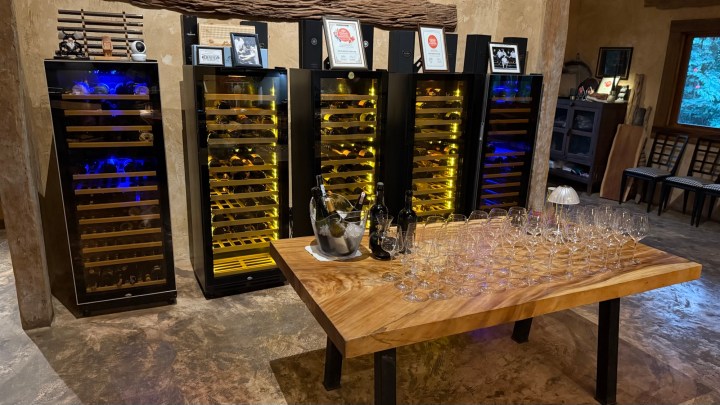 A view of the wine storage area at Locus Native Food Lab, featuring multiple wine refrigerators with illuminated shelves and a wooden table set with wine glasses.
