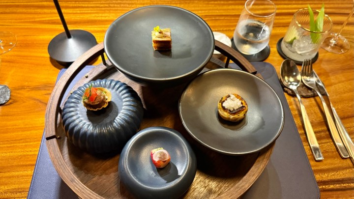 A beautifully arranged selection of amuse-bouche served on a wooden platter with various small plates, featuring intricate garnishes and vibrant colors.