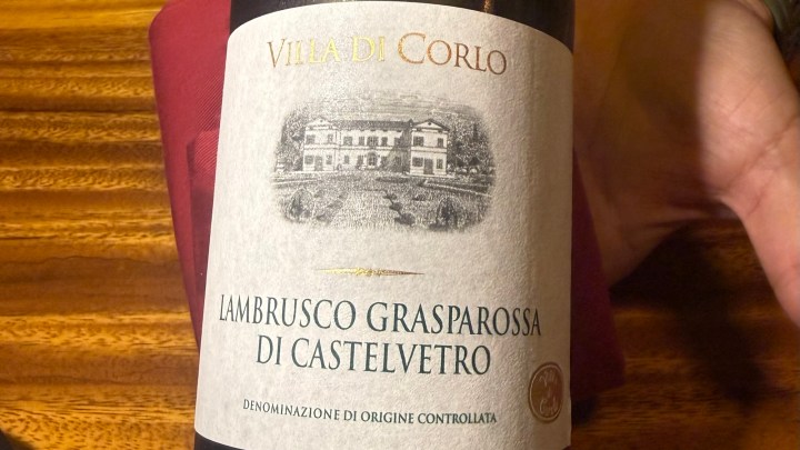 A close-up view of a wine bottle label that reads 'Villa di Corlo Lambrusco Grasparossa di Castelvetro' with a decorative illustration of a landscape.