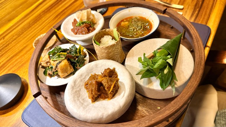A wooden serving tray featuring an assortment of Northern Thai dishes, including various curries, steamed rice, and a selection of herbs and greens.