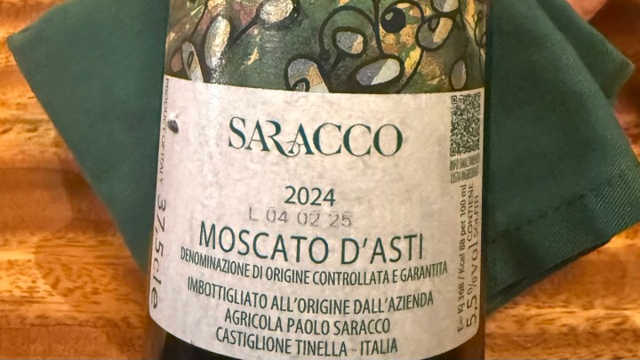 A close-up of a bottle of Saracco Moscato d'Asti, vintage 2024, featuring a colorful label with grape motifs and a green napkin in the background.