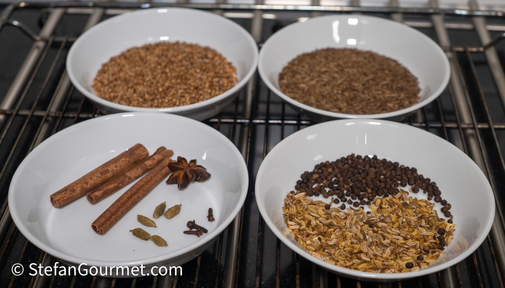 Various spices for curry preparation, including cinnamon sticks, star anise, cloves, cardamom, and cumin, arranged in white bowls.