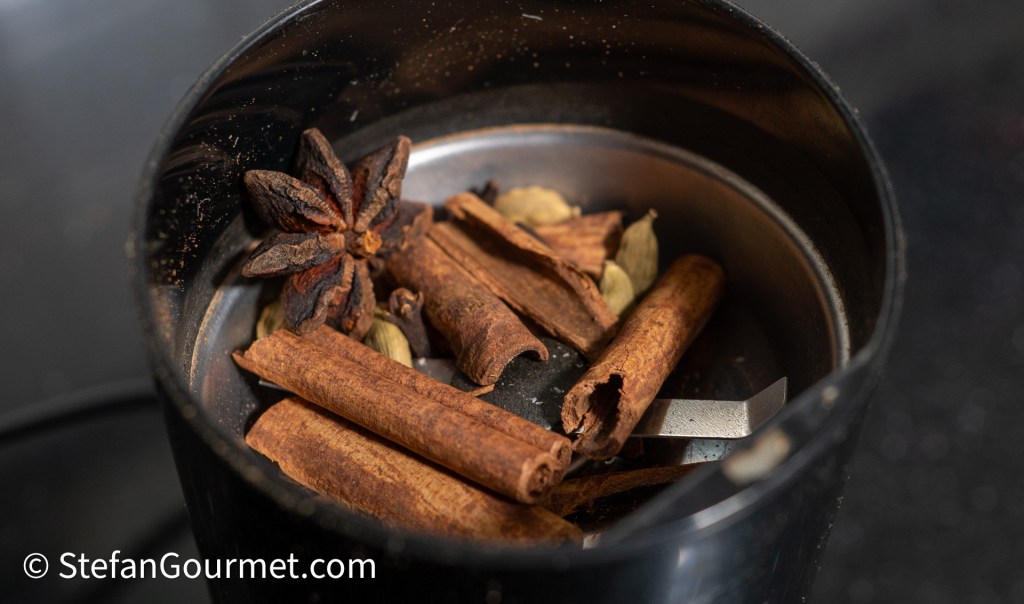Spices including cinnamon sticks, star anise, and cardamom pods inside a spice grinder.