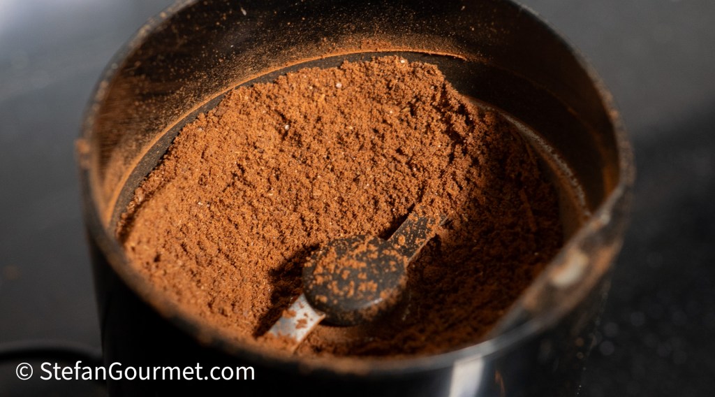 Close-up view of finely ground curry powder in a spice grinder, showcasing a rich reddish-brown color.