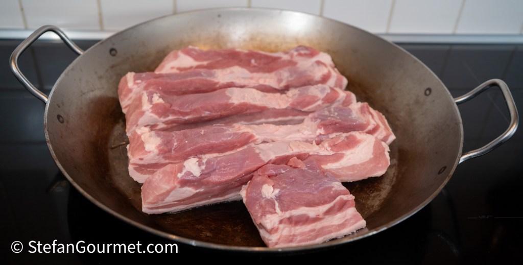 Pork belly slices arranged in a pan, ready for browning.