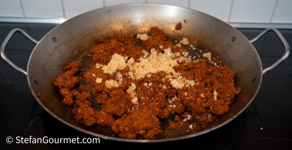 A frying pan with a mixture of brown curry paste and finely grated ginger cooking on a stovetop.
