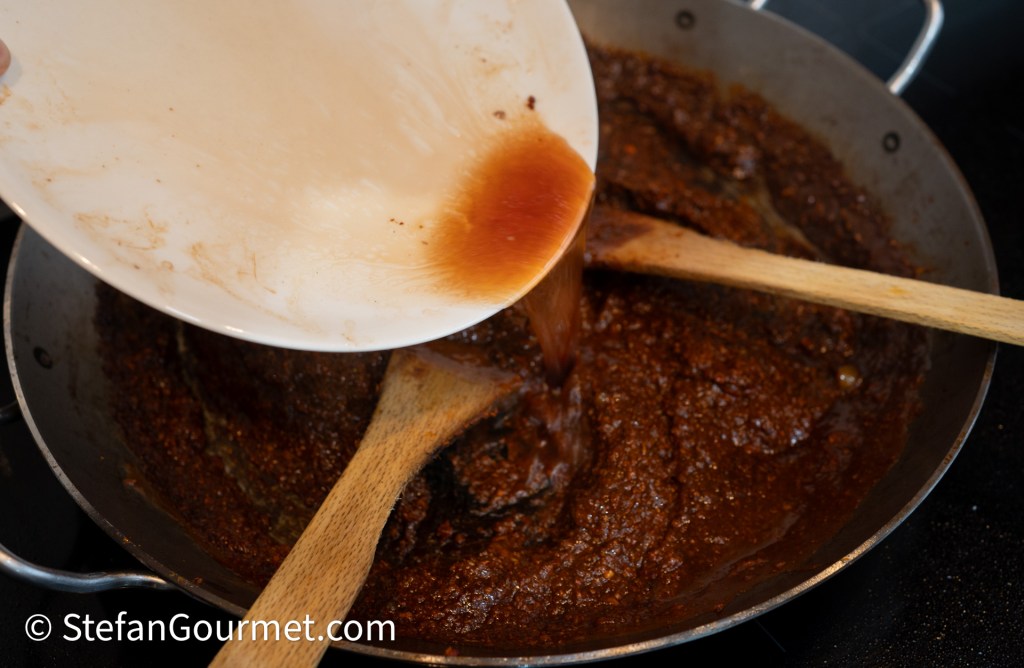 Pouring sauce into a pot of curry while stirring with a wooden spoon.