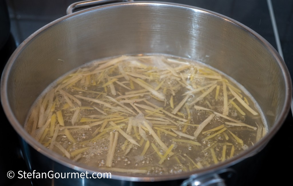 A pot of boiling water with julienned ginger slices floating in it.