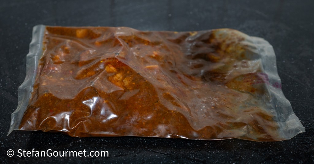 Vacuum-sealed bag containing Gaeng Hung Lay curry, showing the rich brown sauce and pieces of marinated meat.