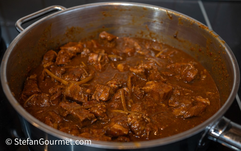 A pot of Gaeng Hung Lay, a Northern Thai curry, with tender chunks of pork simmered in a rich, dark sauce, featuring ginger and spices.