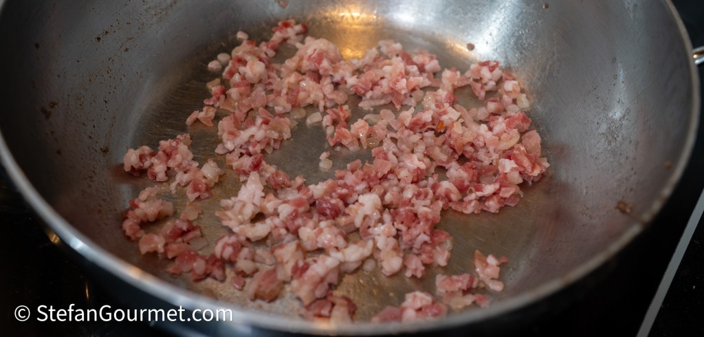 Finely chopped pancetta sizzling in a frying pan.