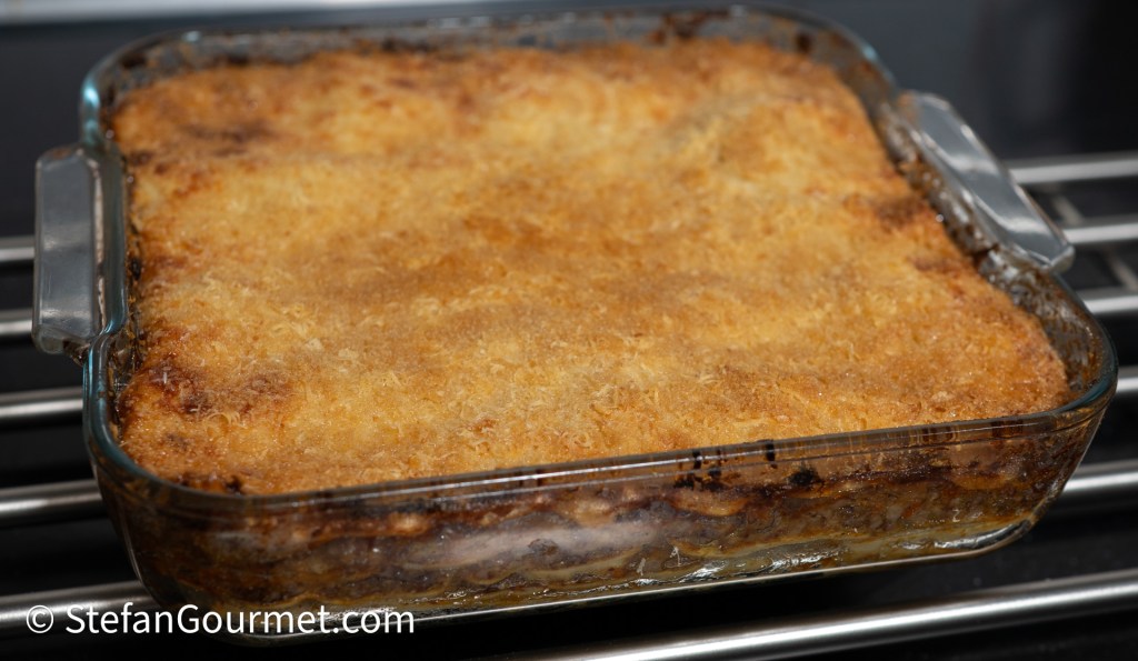 Baked lasagna with a golden, crispy top in a glass dish.