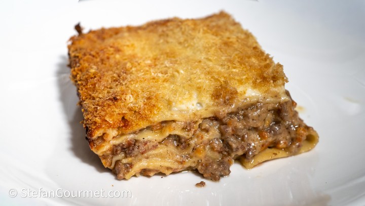 A serving of lasagne al tre carni, showcasing layers of creamy pasta with a golden crust and a rich meat filling.