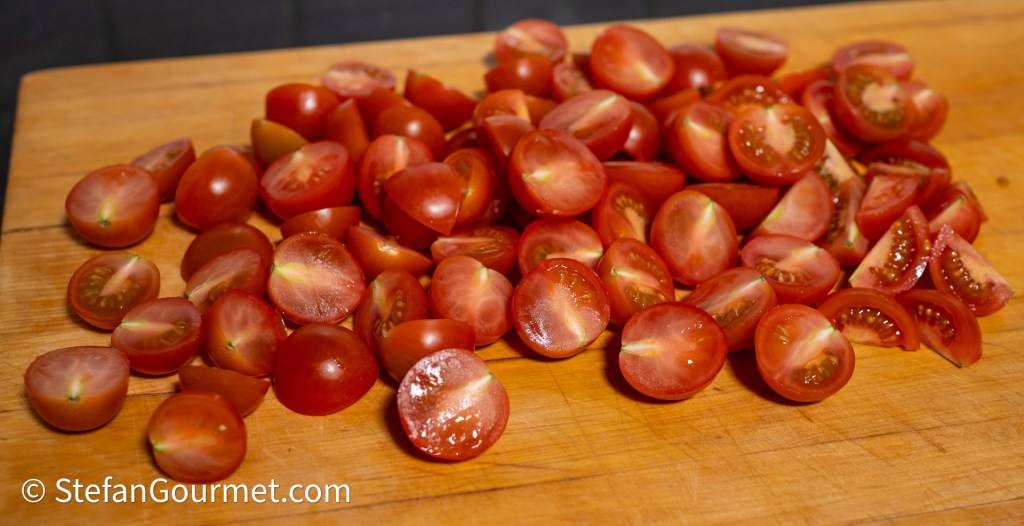 Halved cherry tomatoes arranged on a wooden cutting board.
