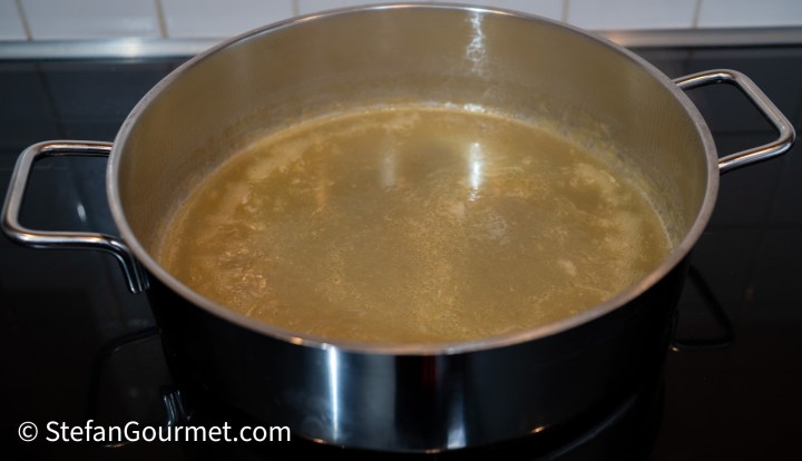 A stainless steel pot filled with fish stock, simmering on the stove.