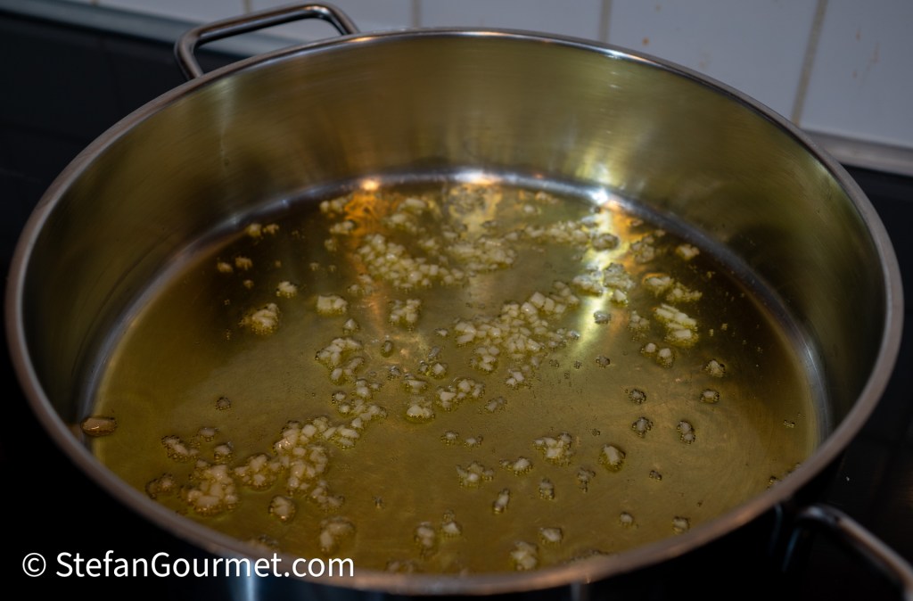 A stainless steel pot with warm olive oil and minced garlic sautéing in it.