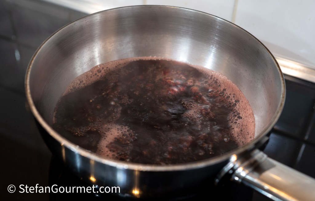 A saucepan with red wine simmering, producing bubbles and steam, on a stovetop.