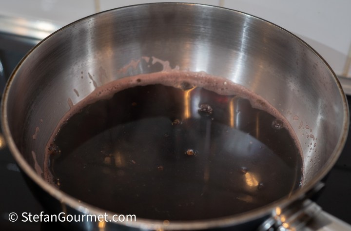 Pot of simmering red wine on the stove, with bubbles forming on the surface.