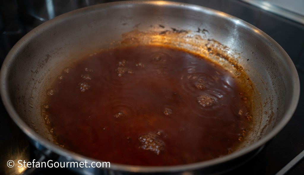 Simmering sauce in a stainless steel pan with bubbles rising to the surface.