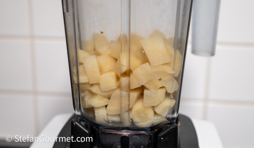 A blender filled with diced pieces of peeled parsley root, ready for blending into a puree.