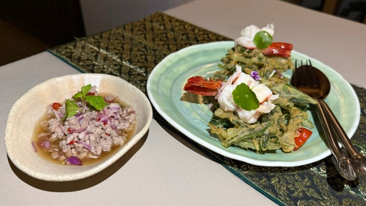 A plate of morning glory tempura features light, crispy fried greens topped with prawns, accompanied by a side of minced chicken salad in a spicy dressing, served on an elegant table setting.
