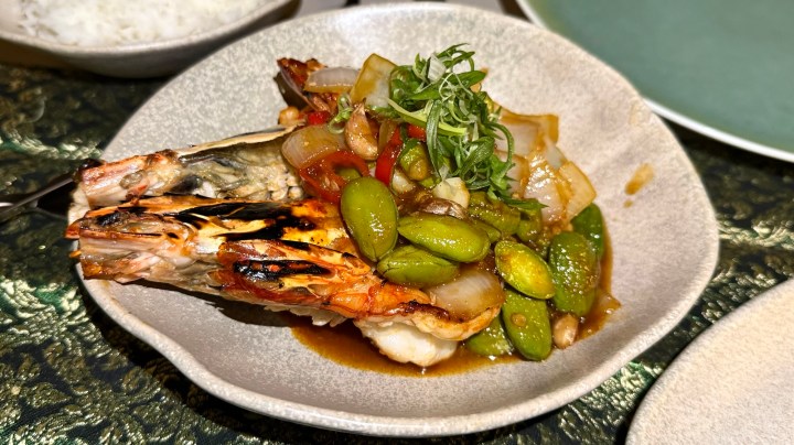 A plate of grilled king prawns served with a sweet and sour sauce alongside 'stinky' beans and diced vegetables, garnished with fresh herbs, and accompanied by a portion of steamed Jasmine rice.