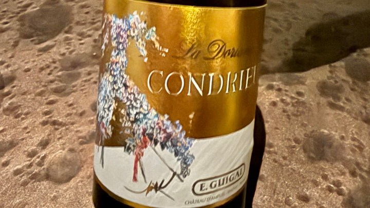 A bottle of Condrieu wine by E. Guigal, featuring a decorative label with floral artwork, placed on a textured surface.