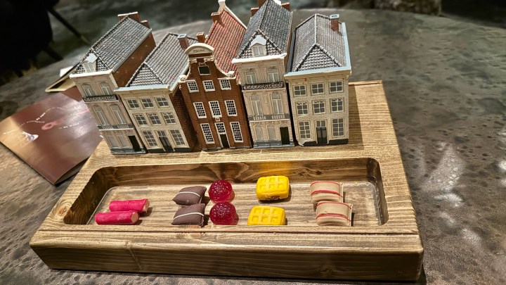 A decorative wooden platter displaying an assortment of colorful desserts arranged alongside a miniature model of traditional Dutch houses.